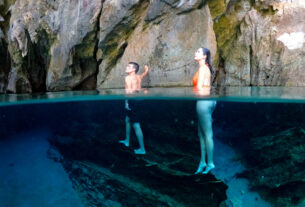 Foto subaquática de um homem e uma mulher escorados nas rochas da gruta da Lagoa do Japonês contemplando o local.