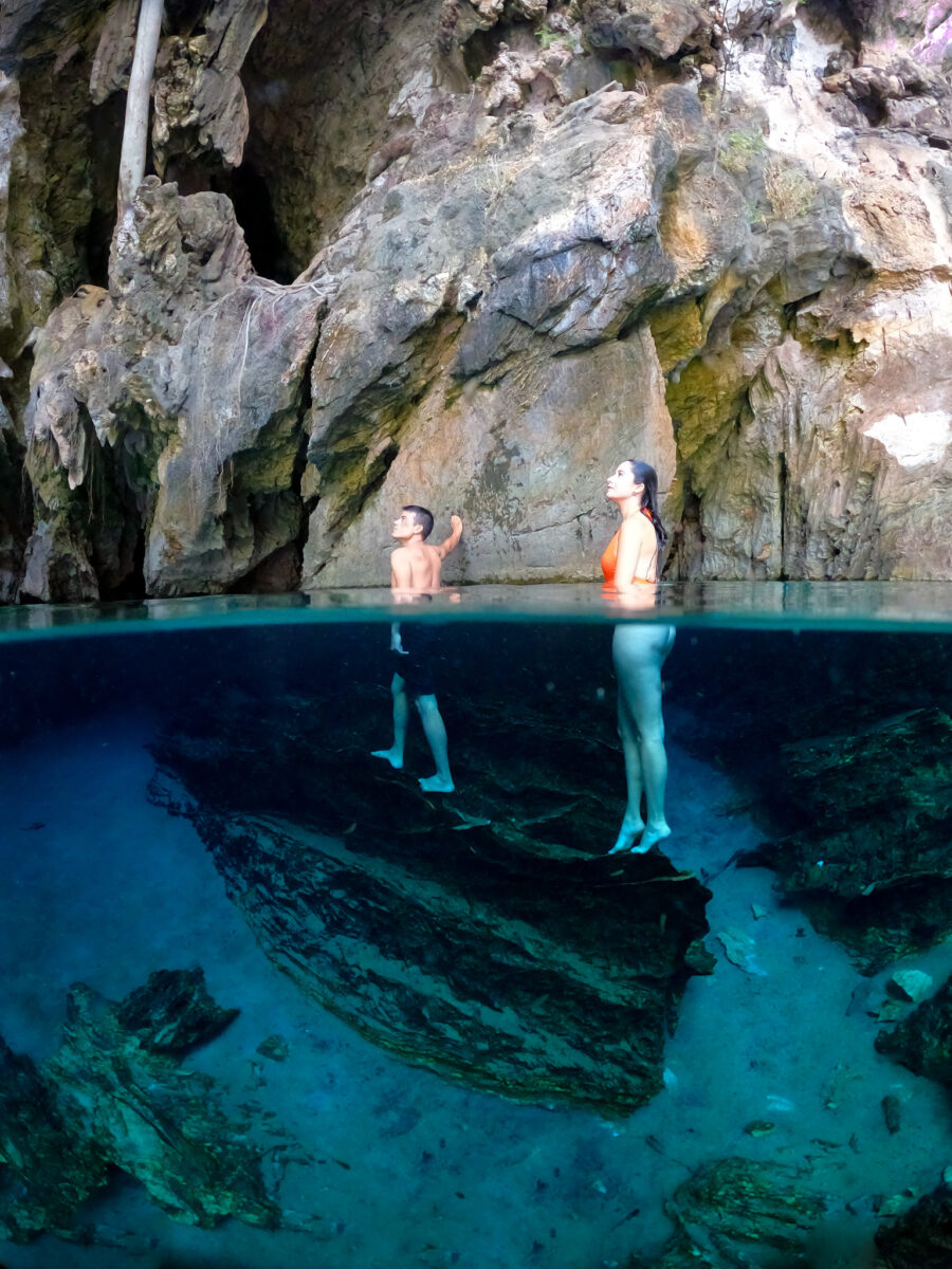 Foto subaquática de um homem e uma mulher escorados nas rochas da gruta da Lagoa do Japonês contemplando o local.